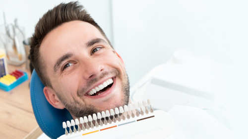 man sitting in dental chair with teeth whitening colour shades