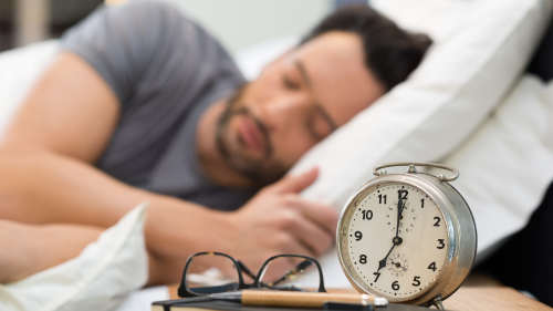man asleep in bed next to alarm clock